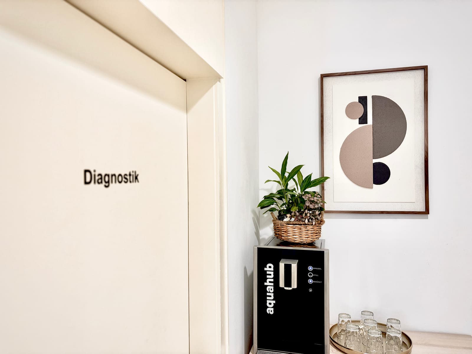 Eingang zum Diagnostik-Bereich mit Wasserspender, Pflanze und ruhigem Kunstdruck